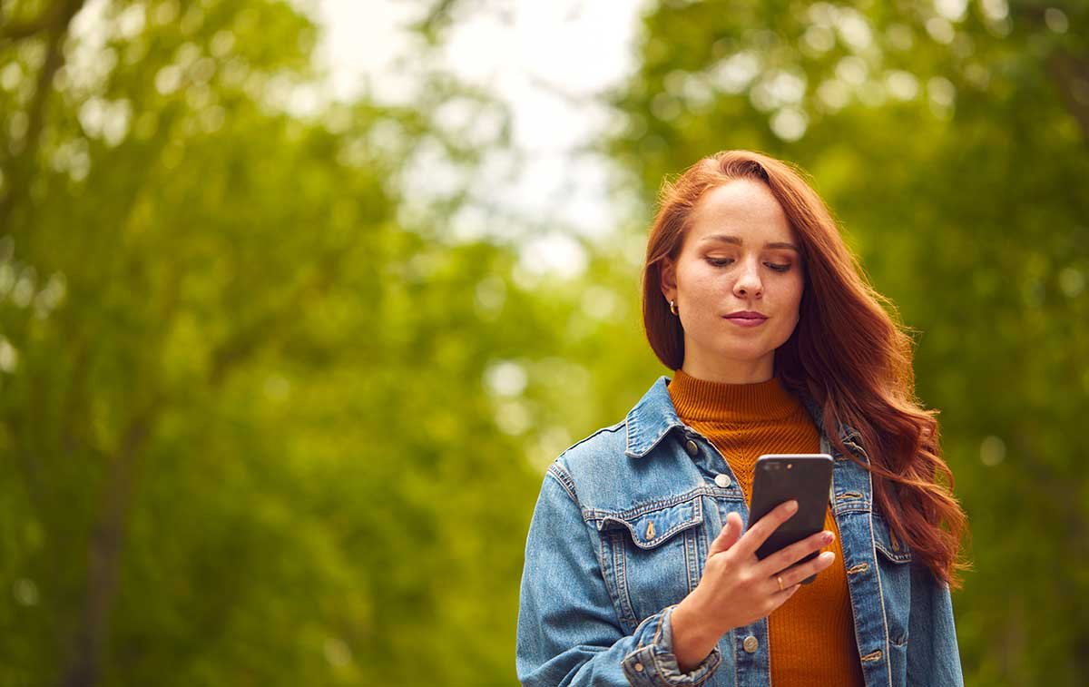 Jeune femme rousse regardant son téléphone dans un parc