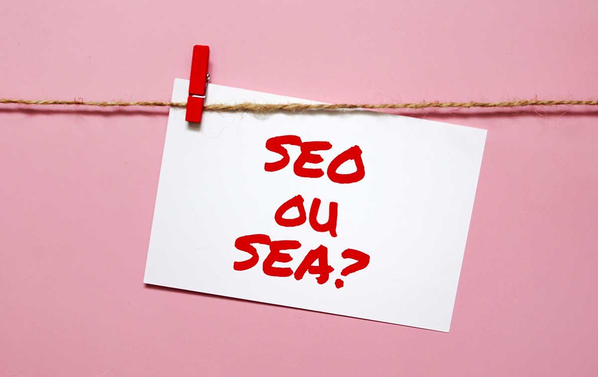 Petit papier sur lequel est inscrit "SEO ou SEA" accroché à une ficelle avec une pince en bois rouge