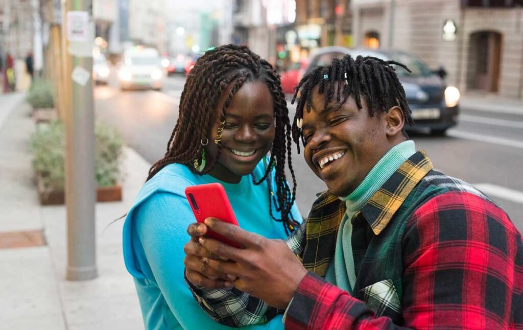 deux jeunes personnes souriantes qui regardent un téléphone dans une rue