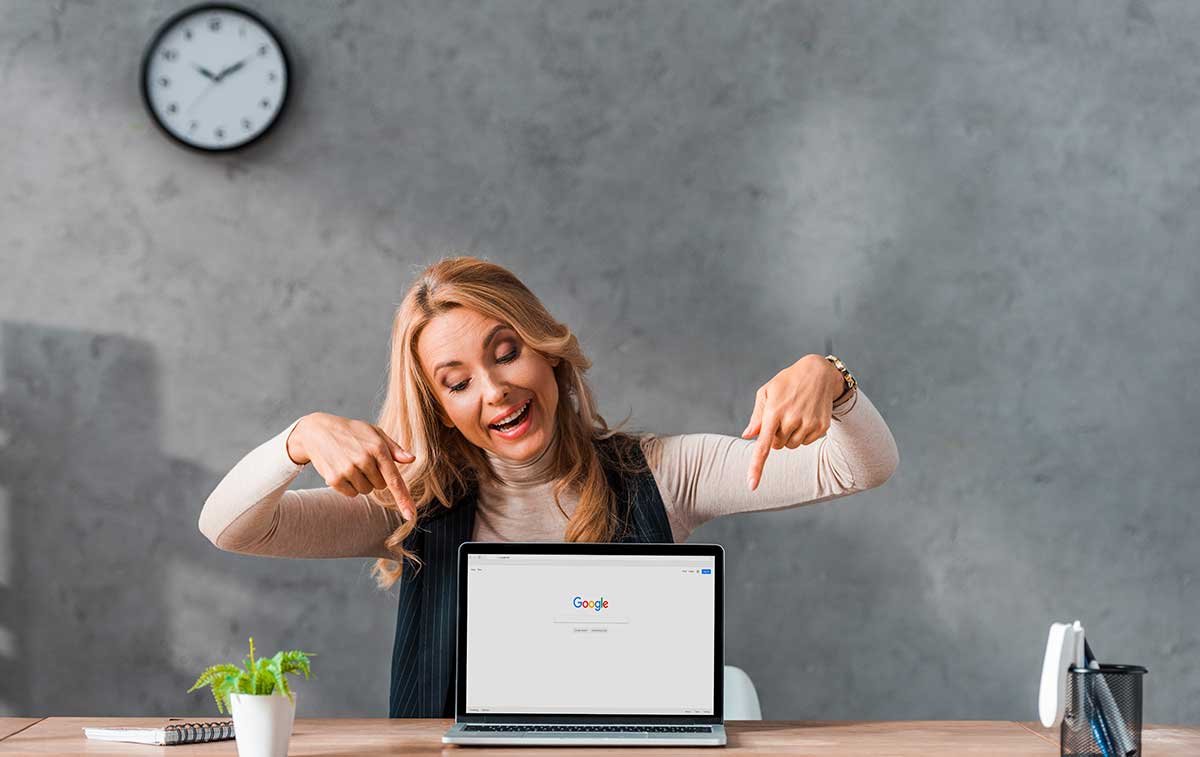 femme blonde souriant qui pointe vers son ordinateur sur lequel est affiché une page google